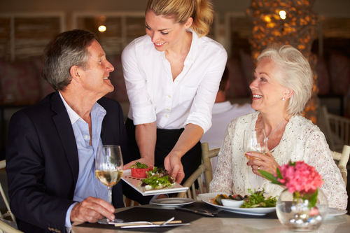 Waitress Serving Food To Senior Couple In Restaurant