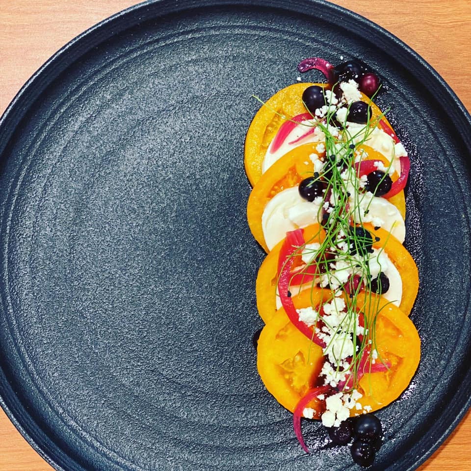 heirloom tomatoes served on a plate with berries cheese and pickled red onions