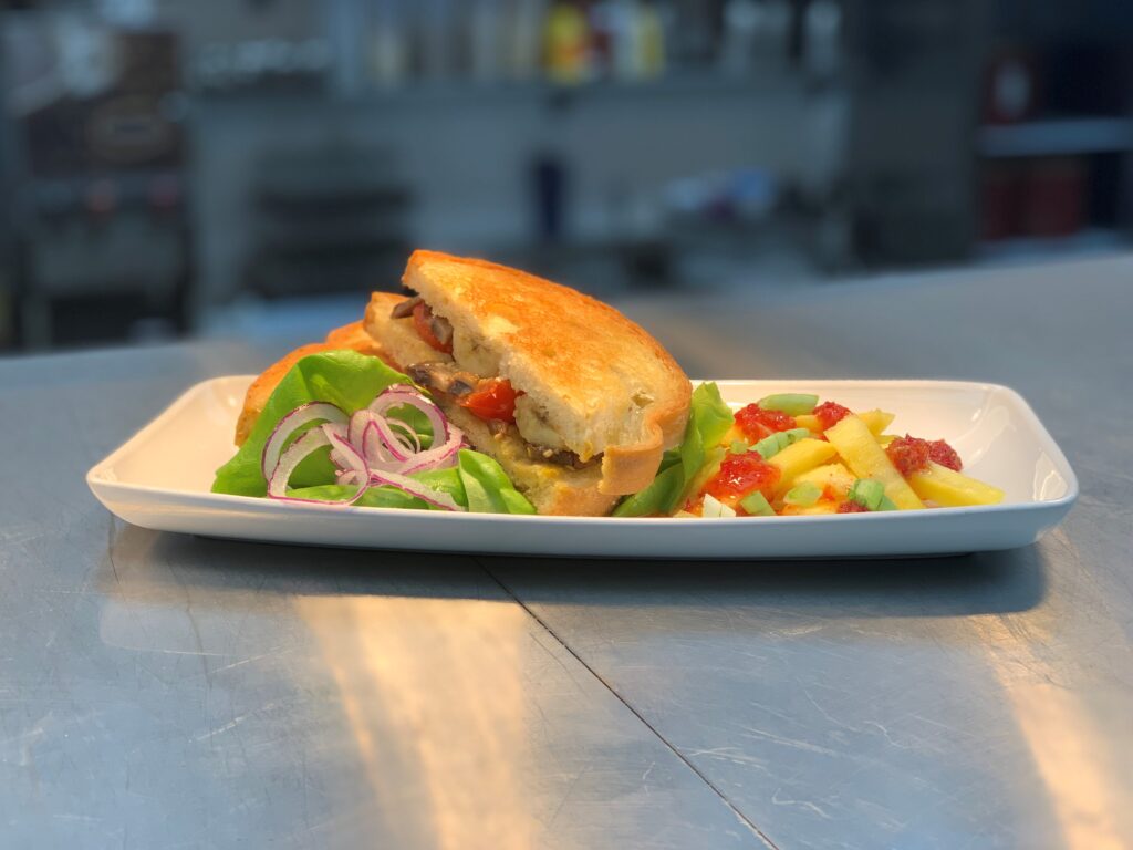 a sandwich with a grilled plantain, lettuce, and tomato served with fruit