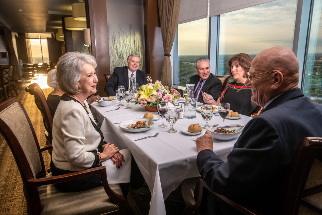 3 men and 2 women senior residents sitting at a formal table eating dinner and conversing