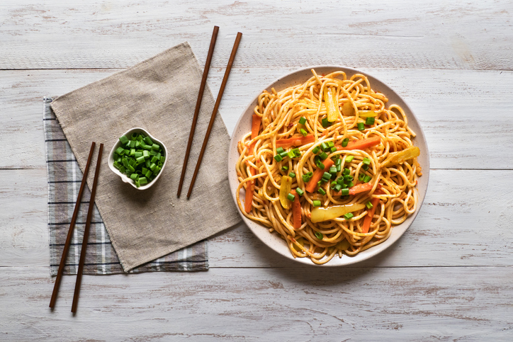 Schezwan Noodles with vegetables in a plate on a white wooden background. Top view.