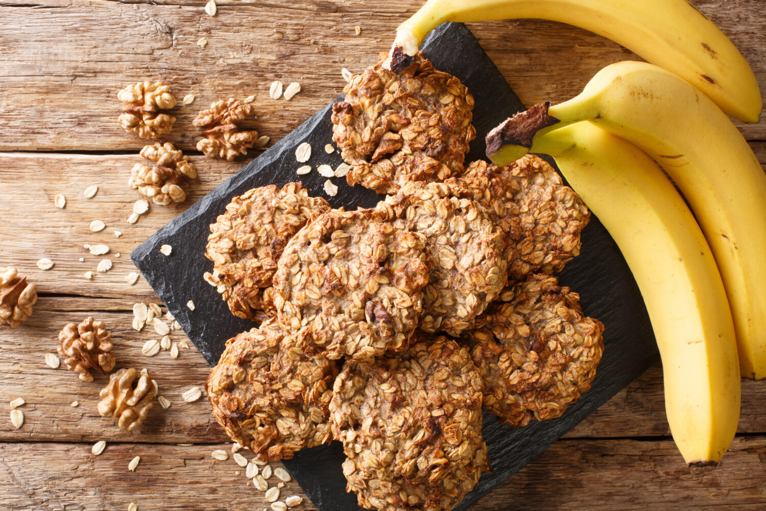 Homemade low-calorie banana cookies with oatmeal and walnuts close-up on a slate board on the table. Horizontal top view from above