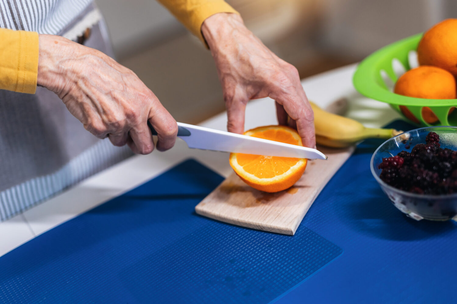 Elderly woman chopping fruits for fresh juice, close up.