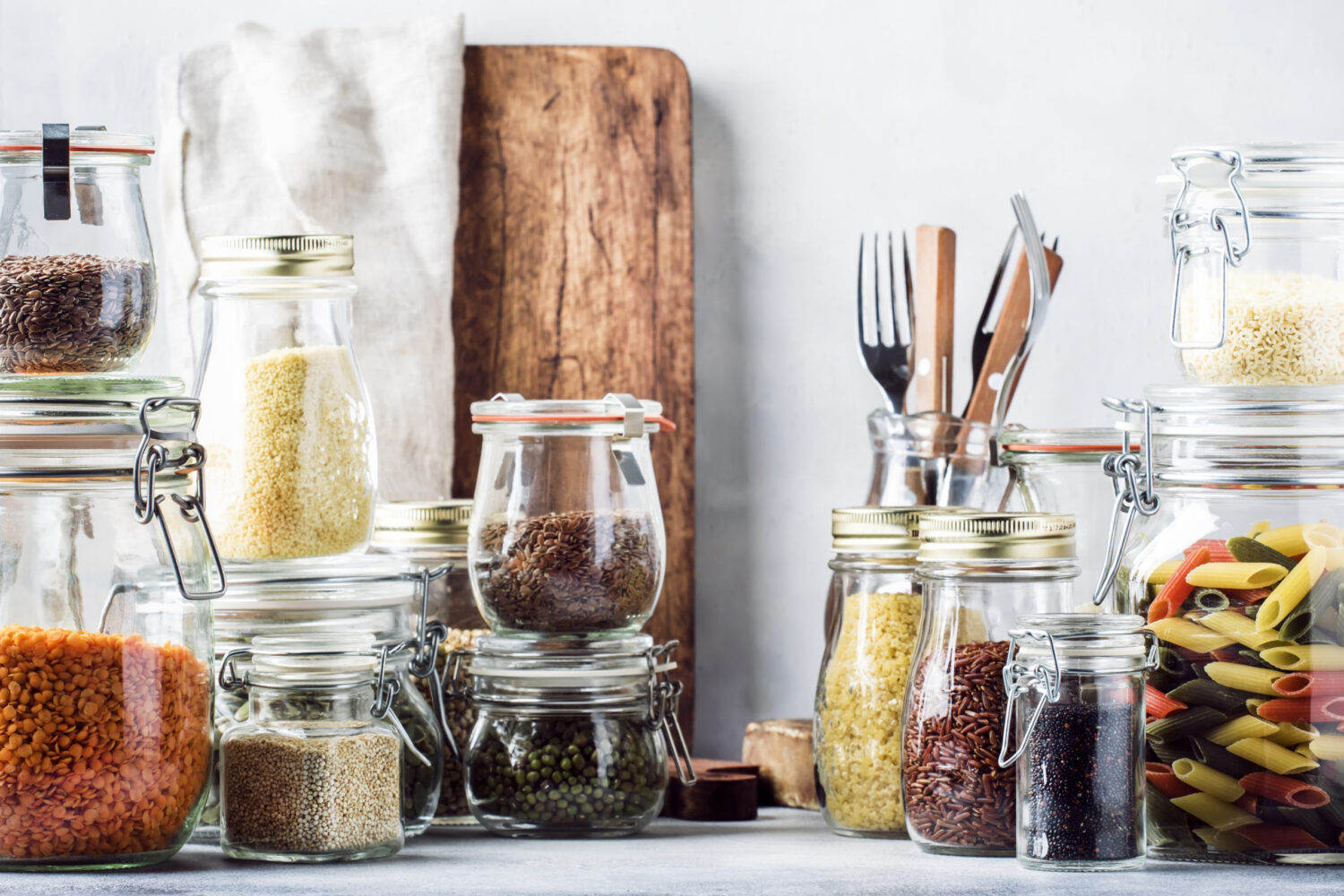 Stocks or set of cereals, pasta, groats, organic legumes and useful seeds in glass jars. Vegan source of protein and energy resources. Healthy vegetarian food. Domestic life scene. Gray kitchen table. Selective focus